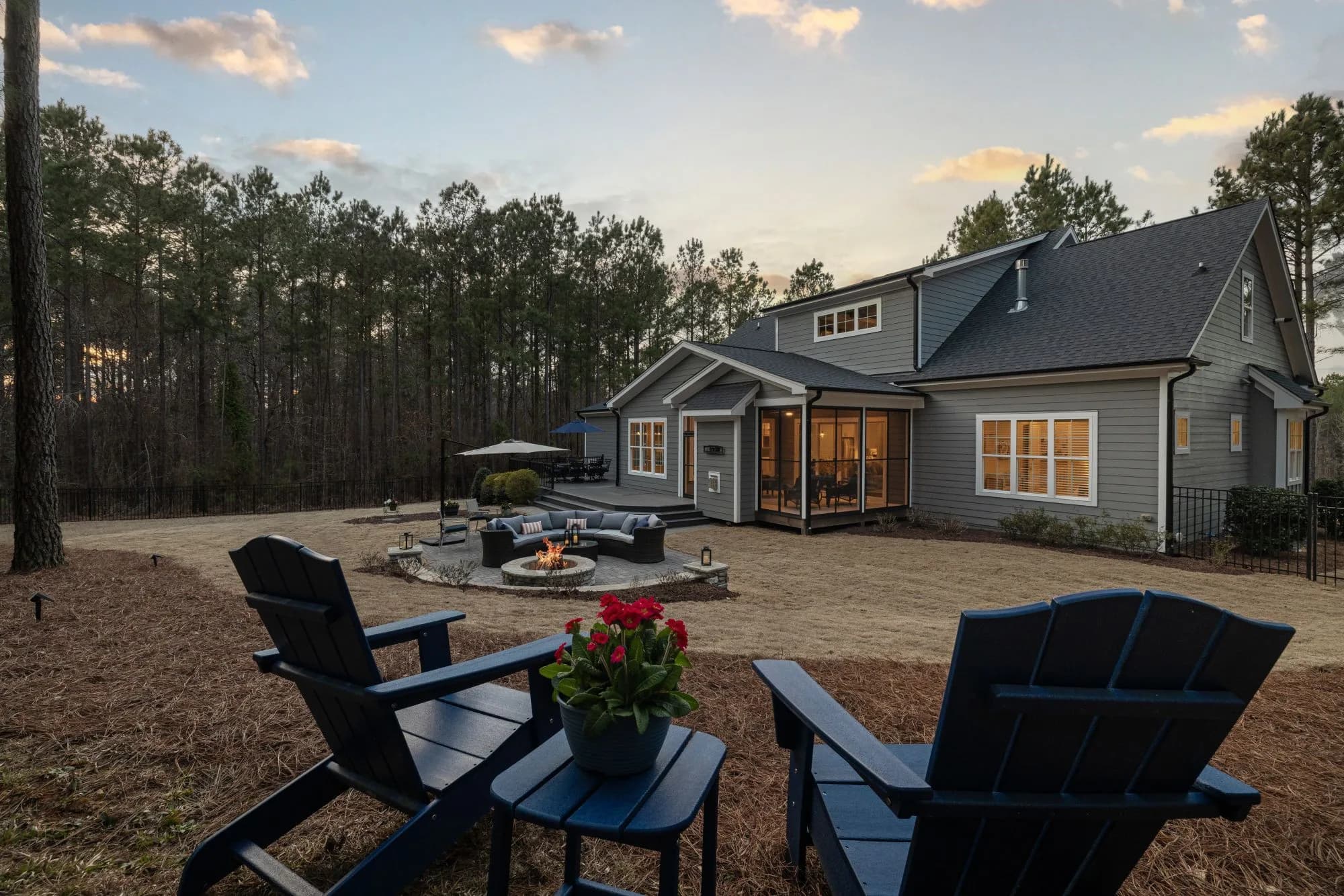 A backyard deck scene with a fire pit, lounge seating and Adirondack chairs at sunset