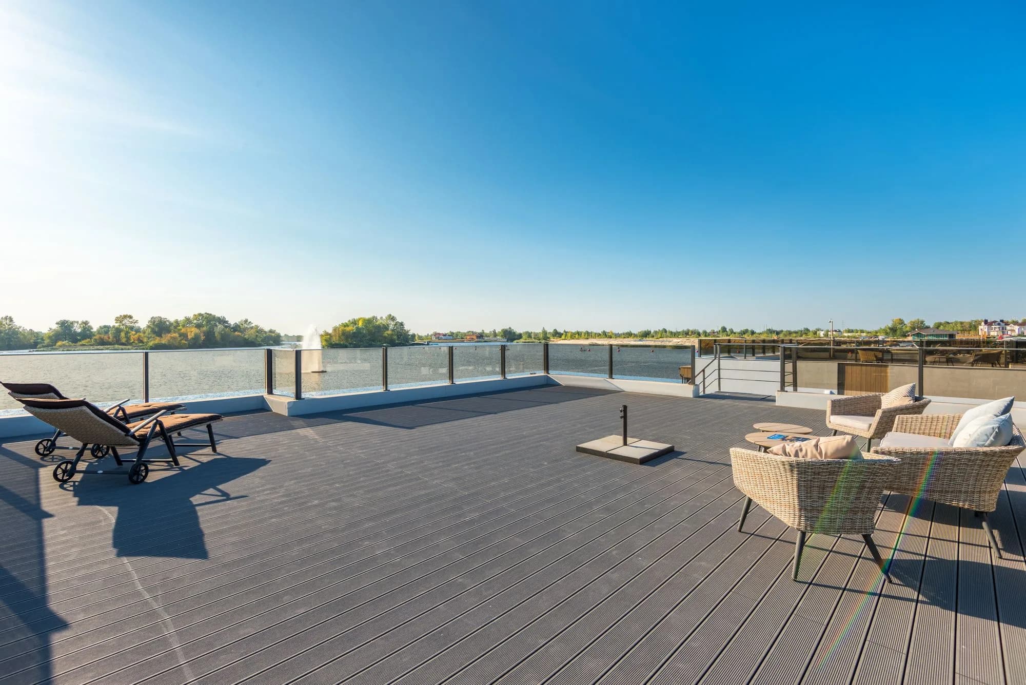 Spacious sunny waterfront deck with modern wicker seating overlooking a lake