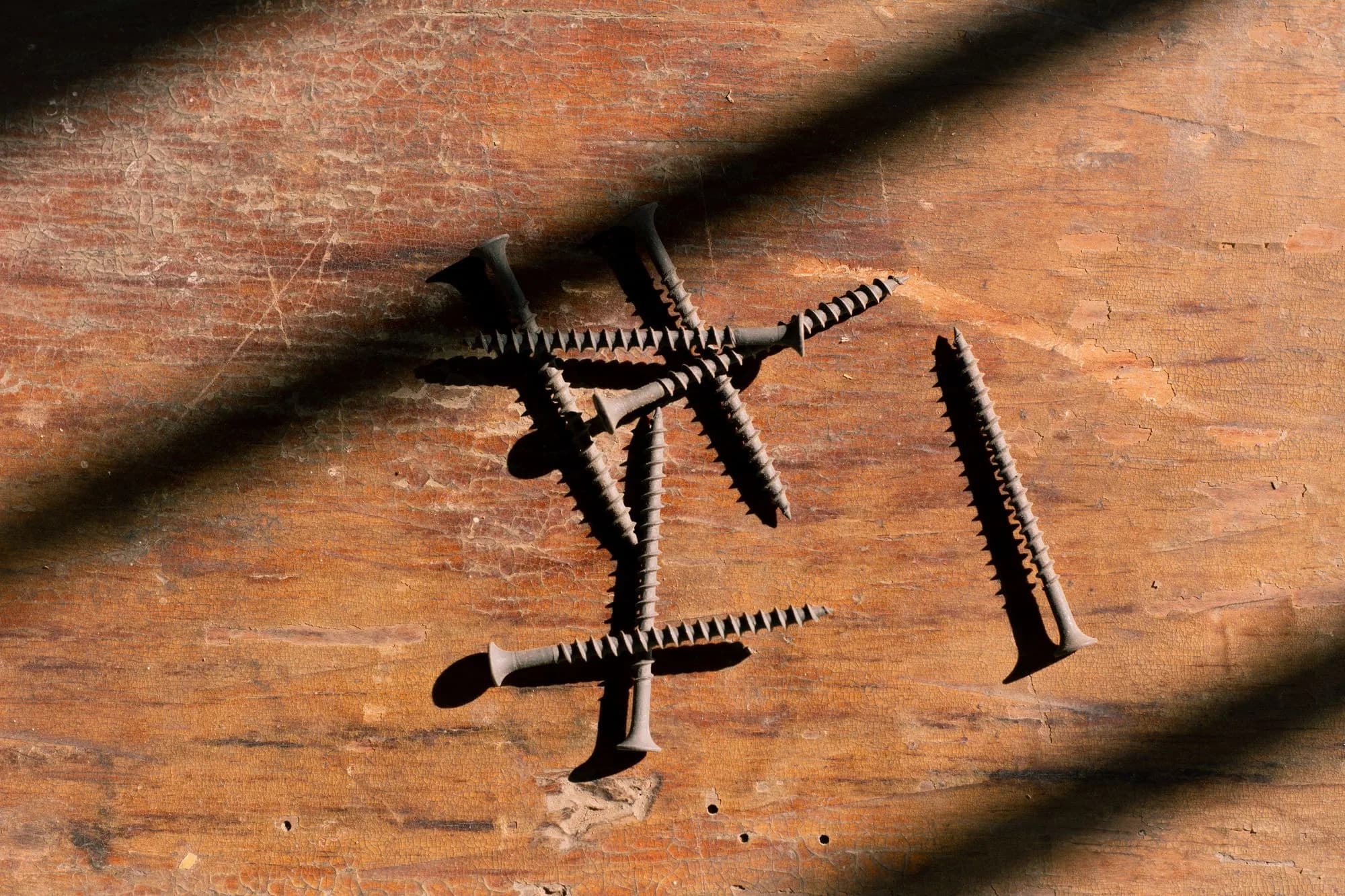 Close-up of deck screws on a wooden surface with dramatic shadow play