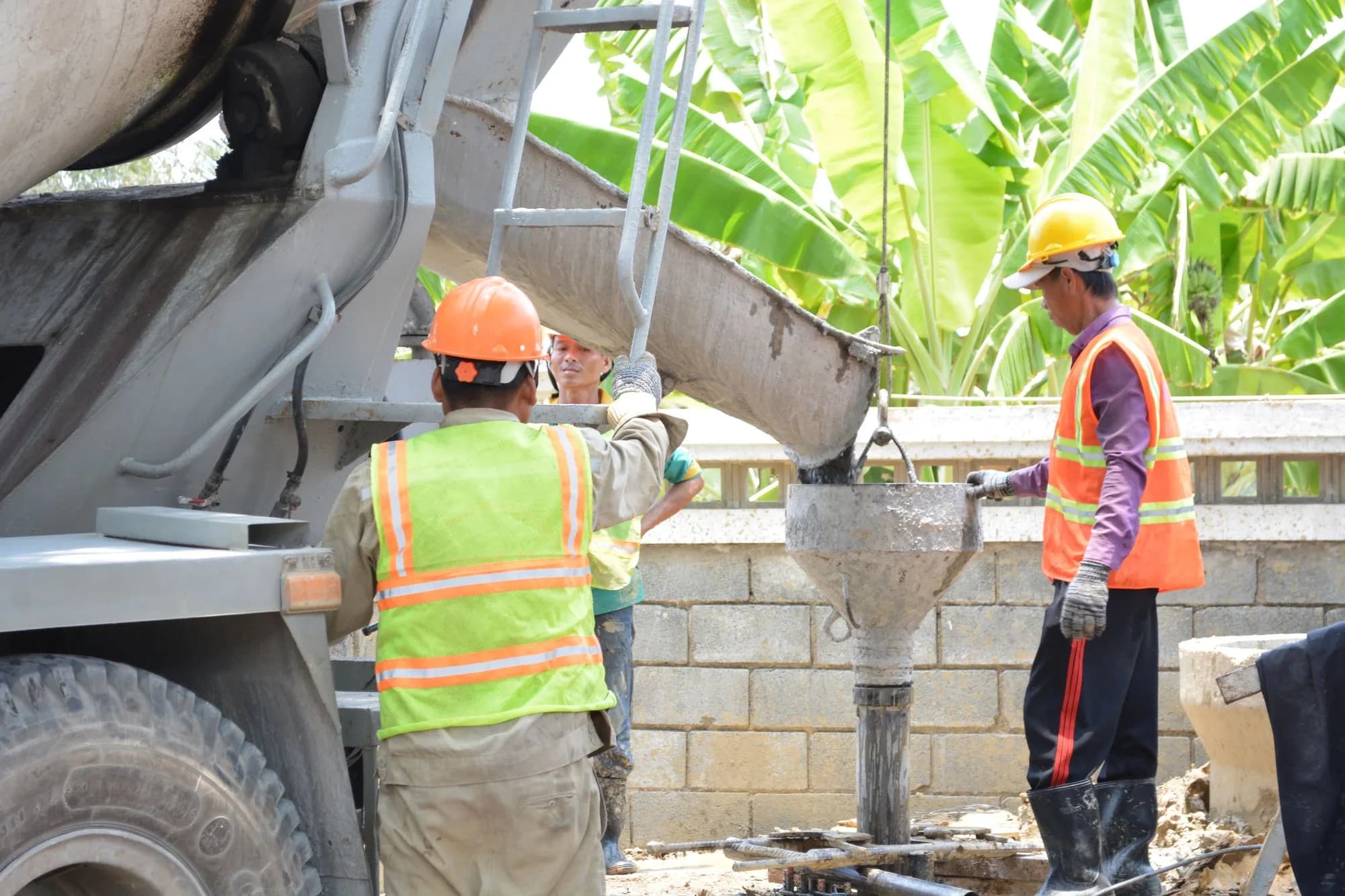 Construction workers in safety gear managing a cement pour from a mixer truck for deck footings
