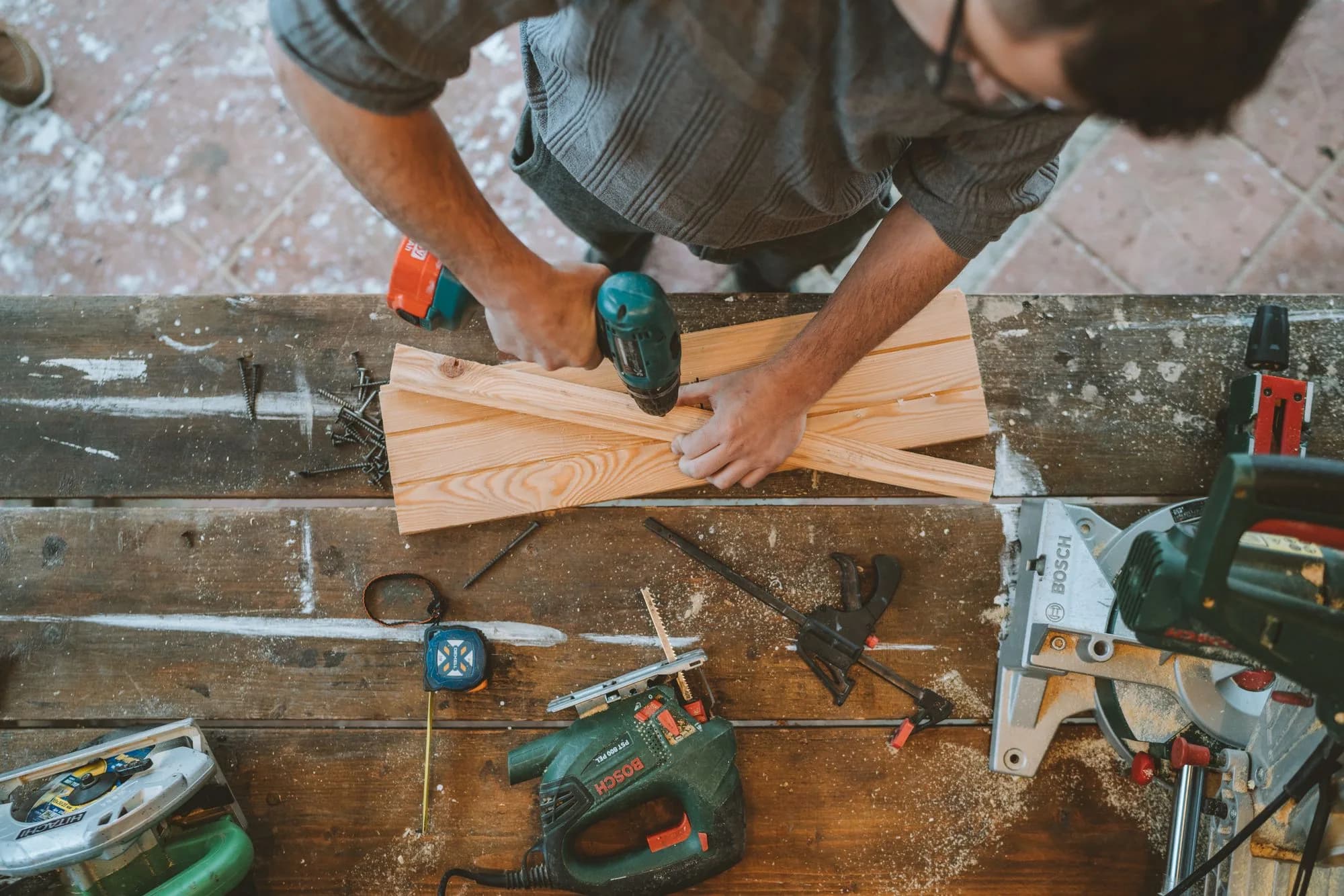 A DIY builder in a home workshop drilling wooden deck planks