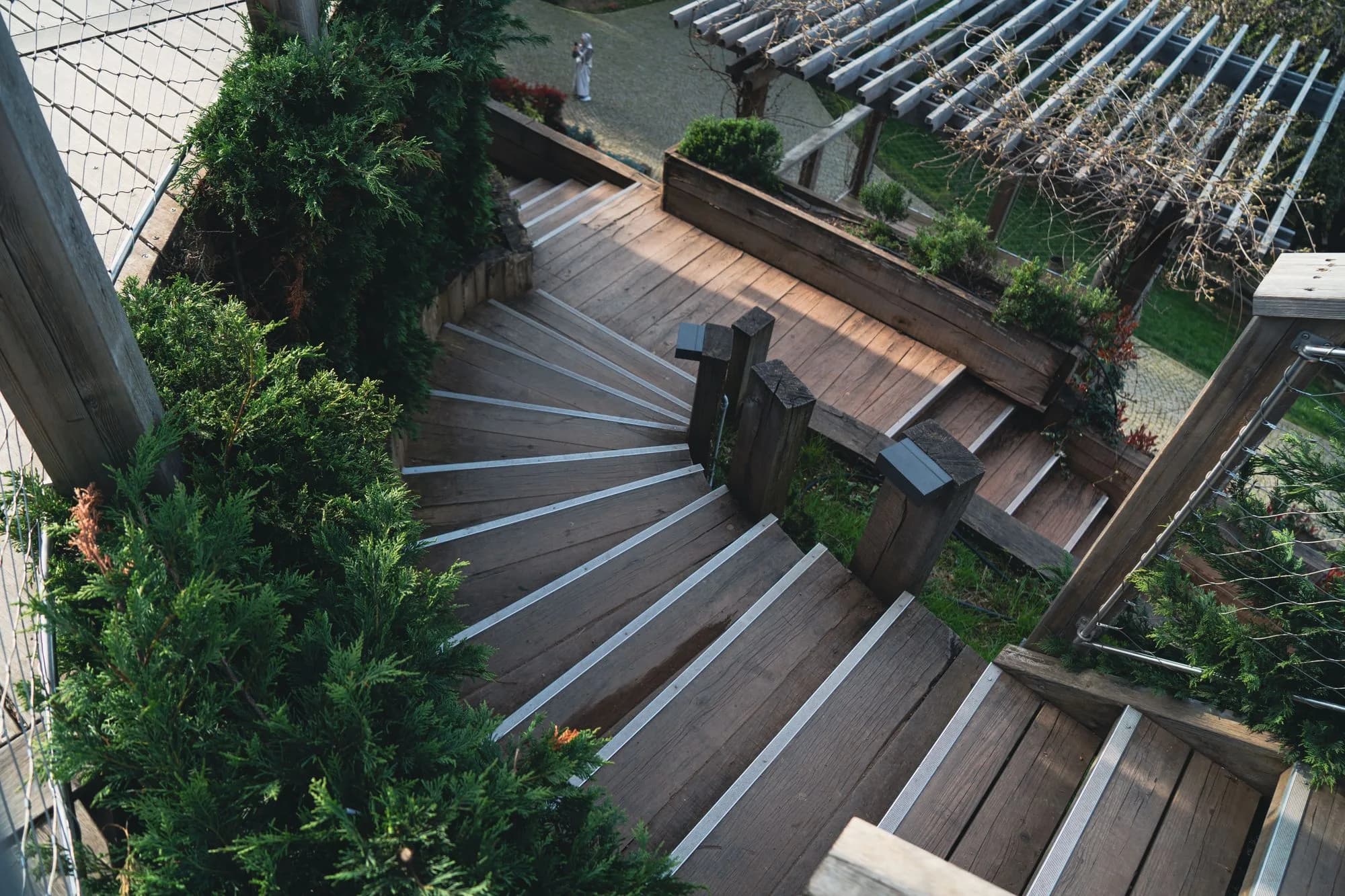 A wooden outdoor staircase framed by lush garden greenery, descending from a raised deck